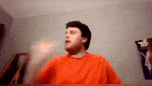 a man in an orange shirt is standing in front of a wall .
