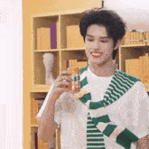 a man wearing a green and white striped scarf holds a can of orange soda