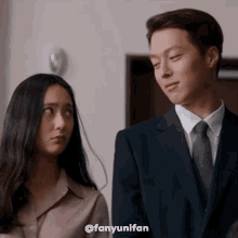 a man in a suit and tie is standing next to a woman in a brown shirt .