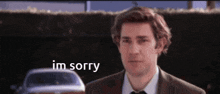 a man in a suit and tie is standing in front of a car and says i 'm sorry