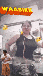 a woman in a black tank top is dancing with the words waasikk behind her