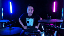 a man in a black shirt with the letter t on it is playing drums