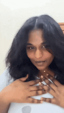 a woman with long black hair is smiling and holding her hands to her chest
