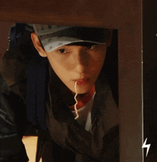 a young man wearing a hat and a leather jacket is looking out from under a table .