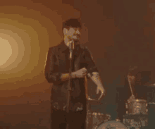 a man singing into a microphone with a drum set in the background