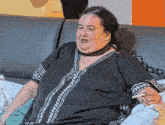 a fat woman is sitting on a couch smoking a cigarette and wearing a choker .