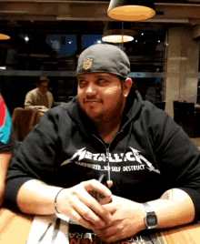 a man wearing a black metallica sweatshirt sits at a table