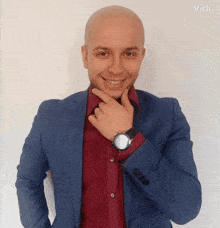 a bald man wearing a blue suit and a red shirt has a watch on his left wrist