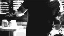 a man in a black t-shirt is standing in a kitchen holding a knife .