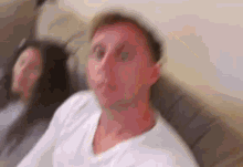 a man and woman are sitting on a couch and the man is making a funny face .