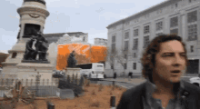 a man with curly hair stands in front of a statue in a city