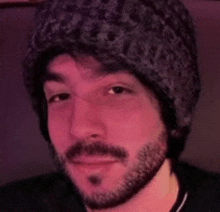 a man with a beard wearing a beanie and a black shirt .