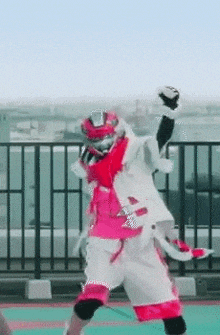 a person in a pink and white costume is standing on a rooftop with their arms in the air .
