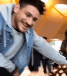 a man in a denim jacket is smiling while holding a piece of food