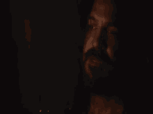 a man with long hair and a beard is standing in the dark looking at something .
