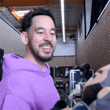 a man with a beard is wearing a purple hoodie and smiling in a room .