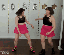 two women in pink skirts are dancing in front of a roar sign