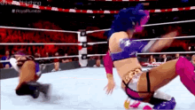 two women are wrestling in a wrestling ring and one of them is falling down .