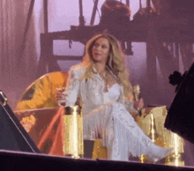 a woman is sitting on a stage holding a microphone and a glass of wine .