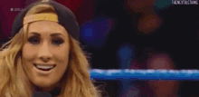a woman wearing a hat and a microphone is smiling in a wrestling ring .