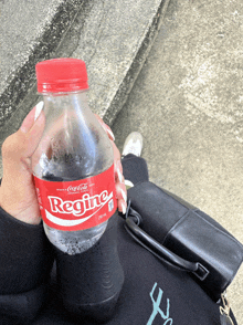 a person holding a bottle of regine coca cola