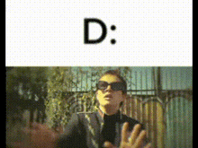 a man wearing sunglasses is standing in front of a fence and the letter d is above him