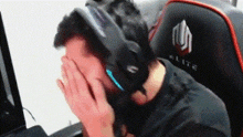 a man wearing headphones is covering his face while sitting in a gaming chair .