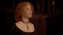 a woman with red curly hair is wearing a choker necklace and a black dress .