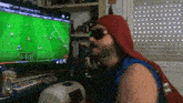 a man wearing sunglasses and a red hat is watching a soccer game on a tv