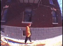 a person walking on a sidewalk in front of a building with a brick wall