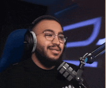 a man with a beard wearing headphones and glasses is smiling in front of a microphone