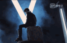 a man in a suit is sitting on a rock in front of a light and a sign that says ioiyi .