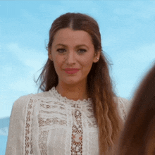 a woman wearing a white lace top looks at the camera