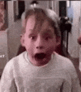 a young boy is making a surprised face with his mouth wide open .