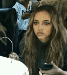 a woman is sitting at a table holding a cell phone and looking at the camera .