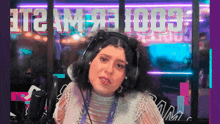a woman wearing headphones stands in front of a neon sign that says it 's am