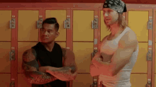 two men are standing next to each other in a locker room . one has a bandana on his head .