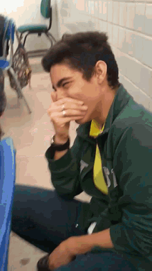 a young man covering his mouth with his hands while wearing a green jacket with the letter r on it