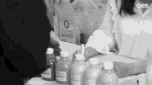 a black and white photo of a woman sitting at a table with bottles of paint .