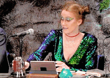 a woman in a sequined dress is sitting at a table with a microphone and a tablet