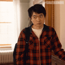 a man wearing a plaid shirt and carrying a backpack has #karatekidmovie written on the bottom