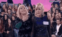 two women are standing next to each other in front of a crowd of people on a television show .