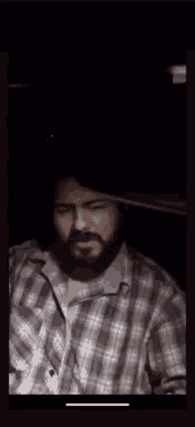 a man with a beard wearing a plaid shirt is standing in a dark room .