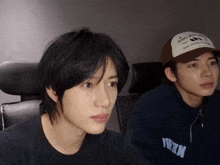 two young men are sitting next to each other and one of them is wearing a baseball cap that says ' new york '