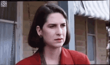 a woman in a red jacket and earrings is standing in front of a building .