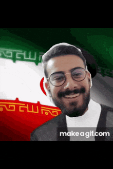 a man with glasses and a beard is smiling in front of a flag