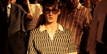 a man wearing sunglasses and a black and white shirt stands in a crowd