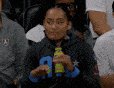 a woman in a black sweatshirt with the letter a on it holds a green bottle