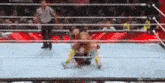 a referee is standing in the middle of a wrestling ring watching a match .