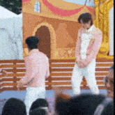 a man in a pink jacket and white pants stands on a stage